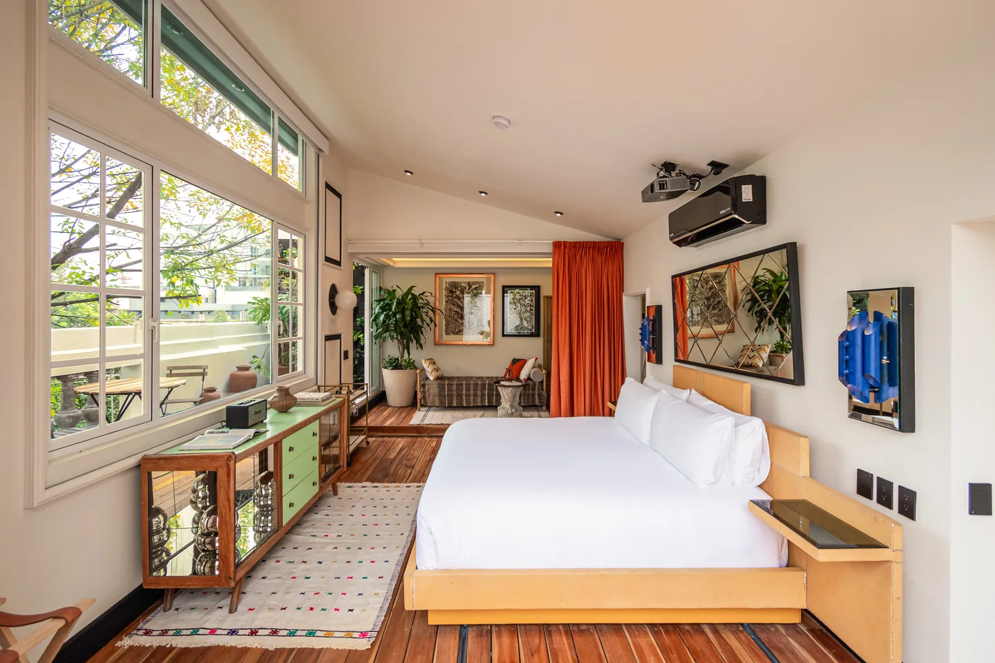 Bedroom with a wall of windows onto the treetops and orange curtains — Cilene Suite, La Valise Mexico City