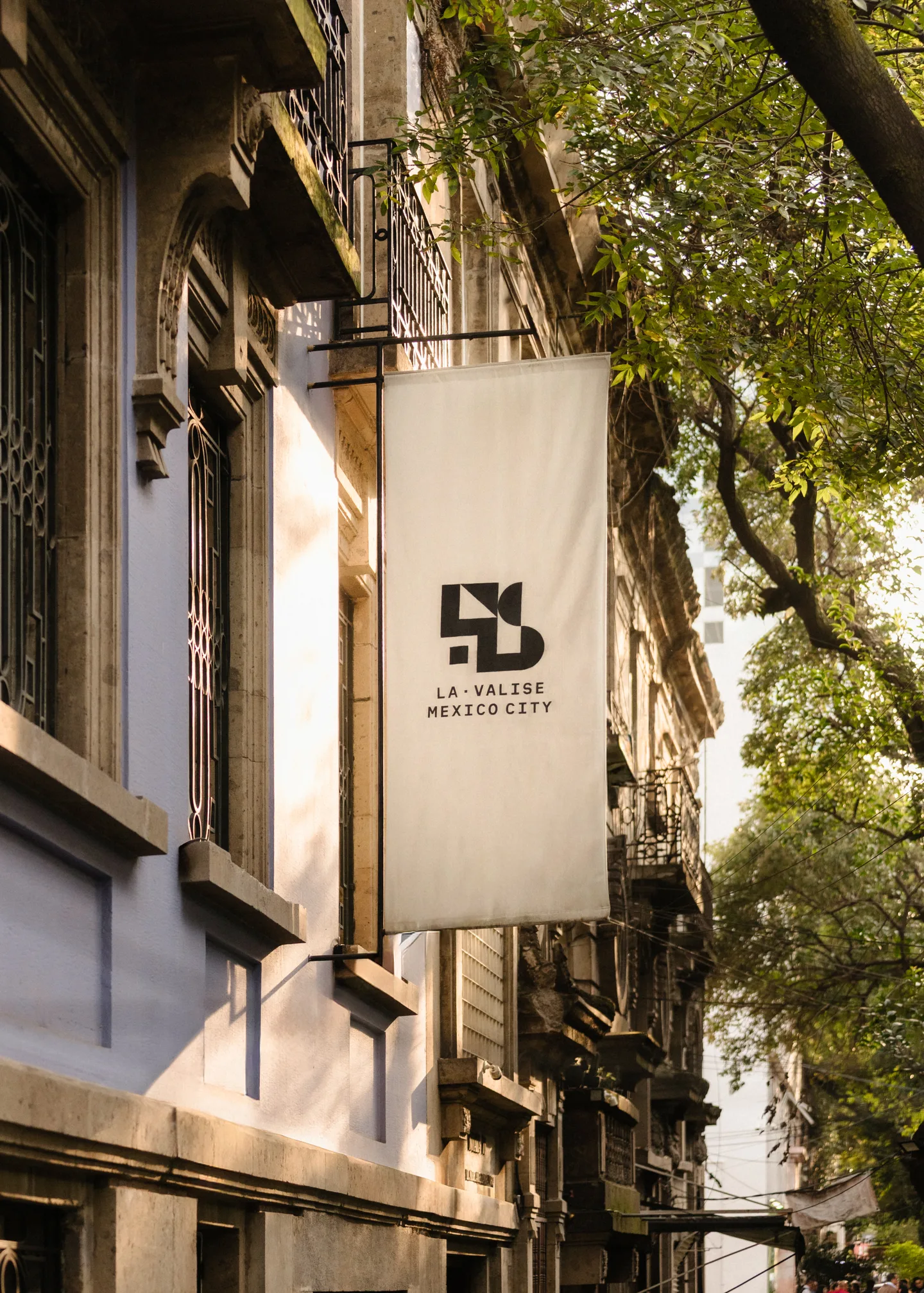 White La Valise banner sign hanging from the townhouse façade on a tree-lined street in Roma Norte
