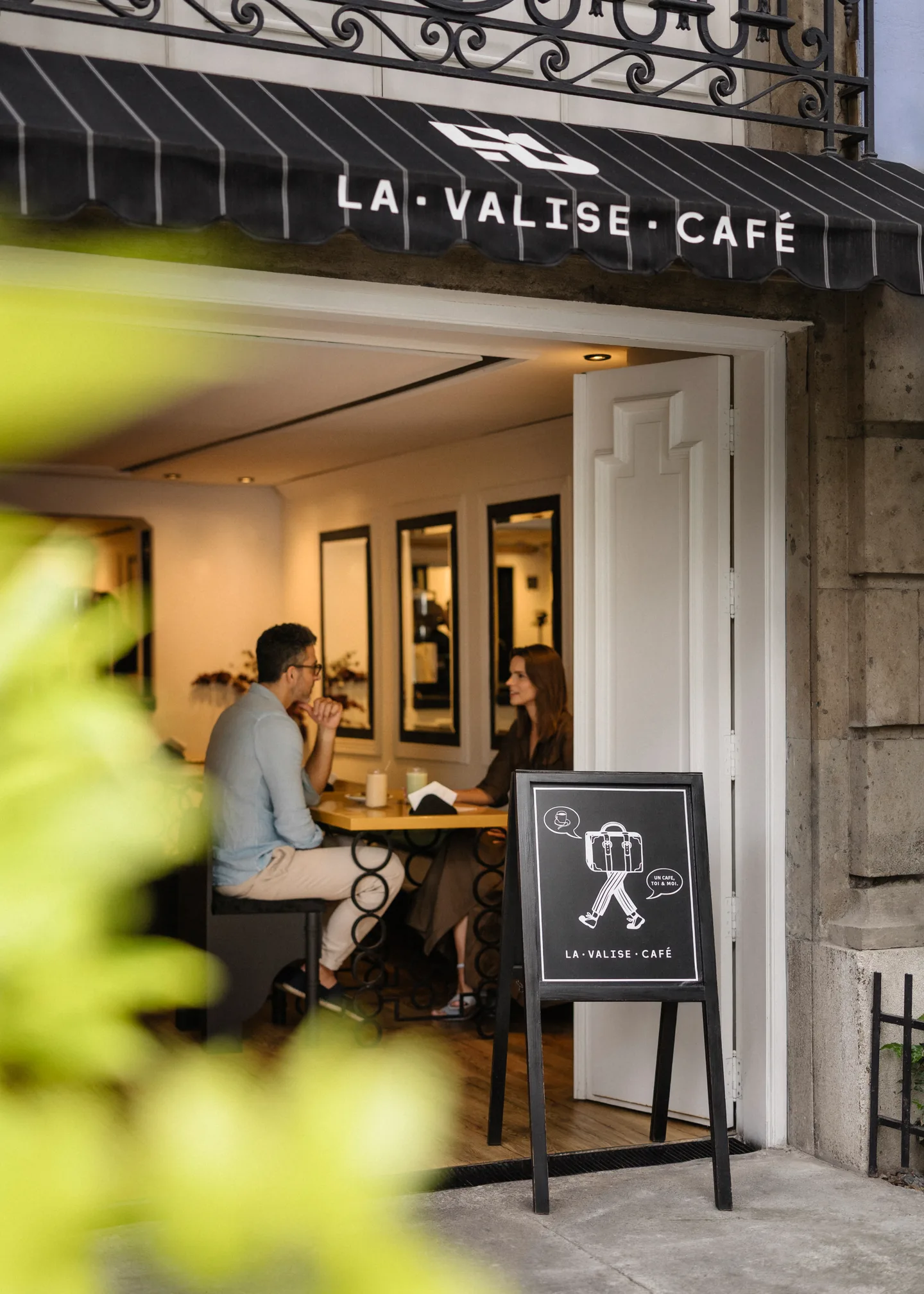 Guest having coffee at the street-side entrance of La Valise Café in Roma Norte, with a chalkboard menu by the door
