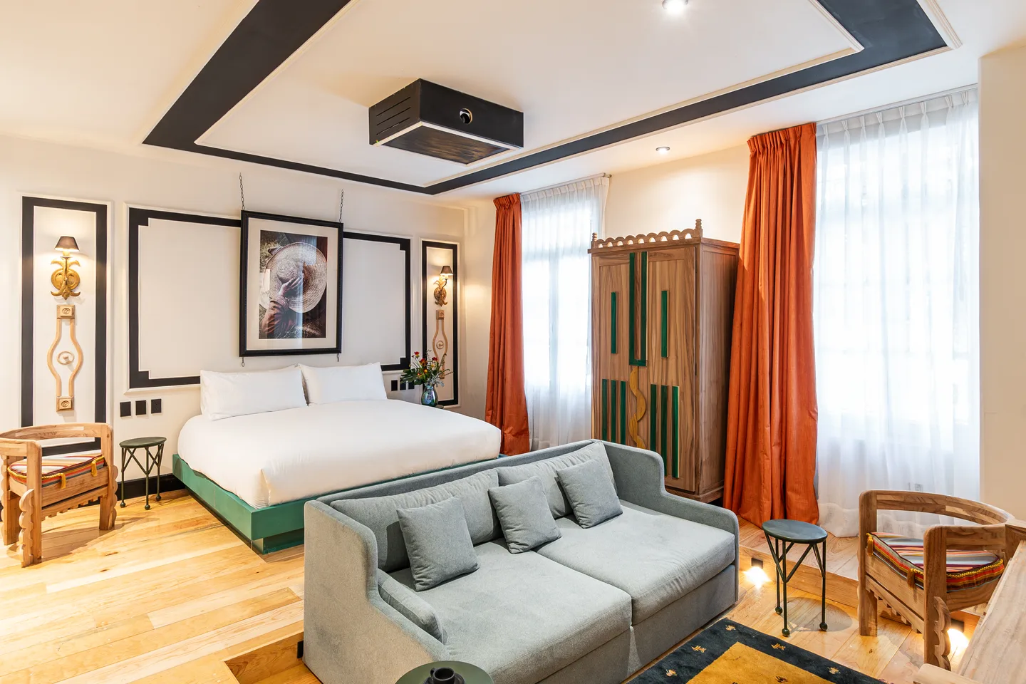 Bed and grey sofa beneath the ceiling projector, with orange curtains — Nova Suite, La Valise Mexico City